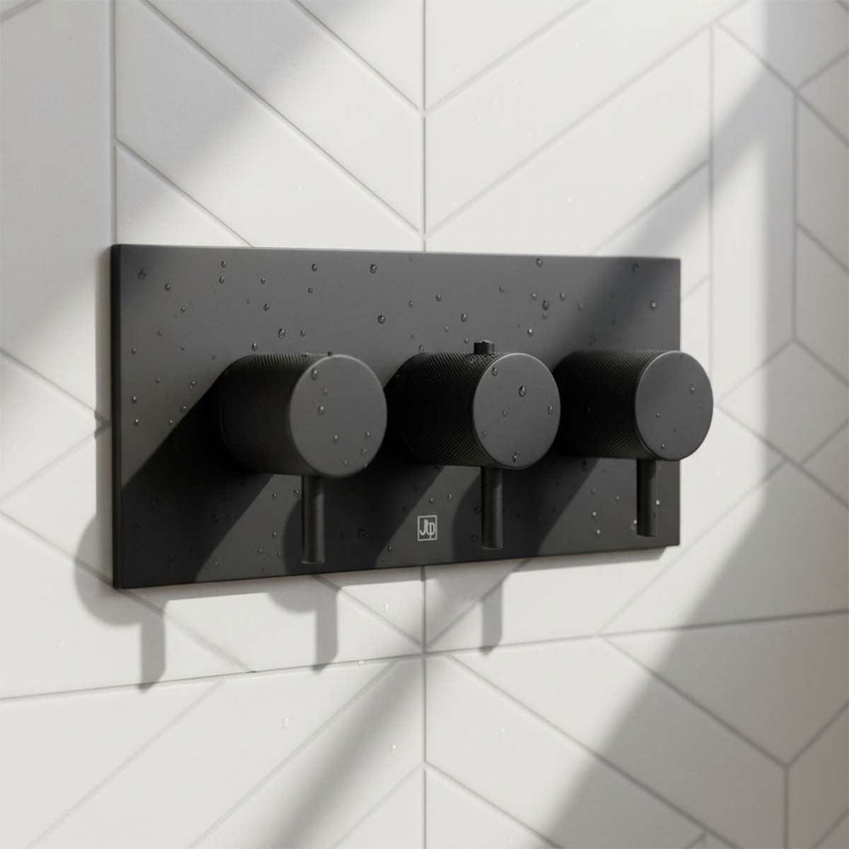 matt black three-hole shower control trim set mounted on a white geometric tiled wall, with water droplets visible on the surface.
