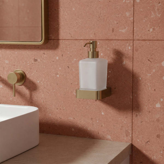 A frosted glass soap dispenser with a brushed gold pump and mounting bracket, 1200