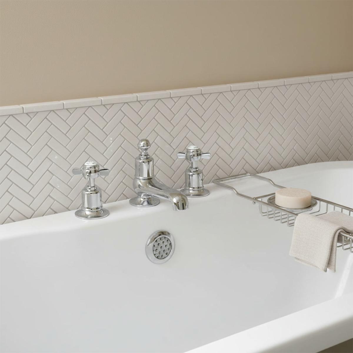 A polished chrome three-hole bathroom tap set with cross handles installed on a white bathtub
