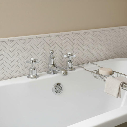 A polished chrome three-hole bathroom tap set with cross handles installed on a white bathtub 1200