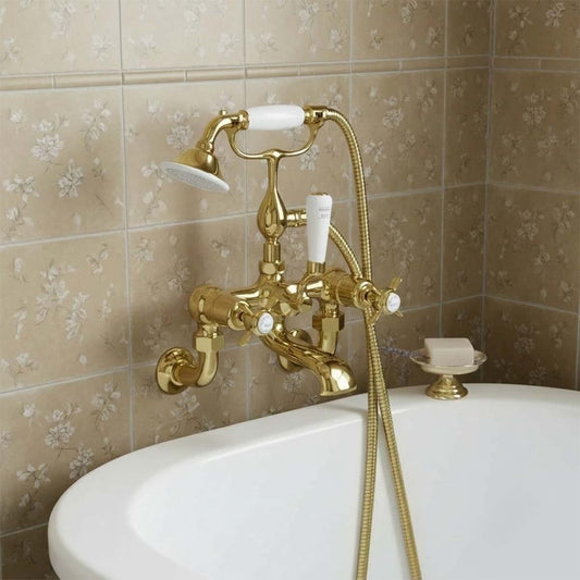 A vintage-style brass bathtub faucet set with white ceramic handles and a handheld shower attachment, mounted on a tiled wall above a white bathtub. 1200