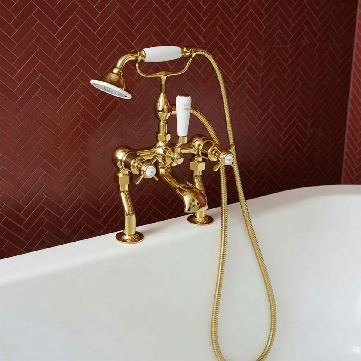 A vintage-style brass bathtub tap set with a handheld shower attachment, mounted on the edge of a white bathtub