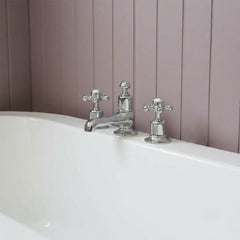 polished chrome three-hole bathroom faucet set with two cross handles installed on the rim of a white bathtub